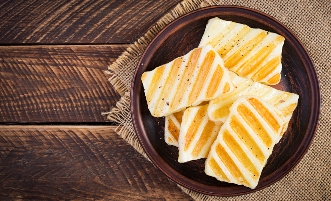 Fa asztalon egy tányér, azon grillsajt szeletek.