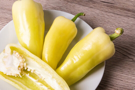 A képen egy fehér tányéron 3 darab egész, és egy félbevágott paprika van.