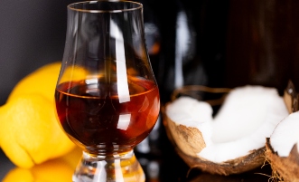 Egy pohárban rum van, a háttérben pedig narancs és kókuszdió látható.