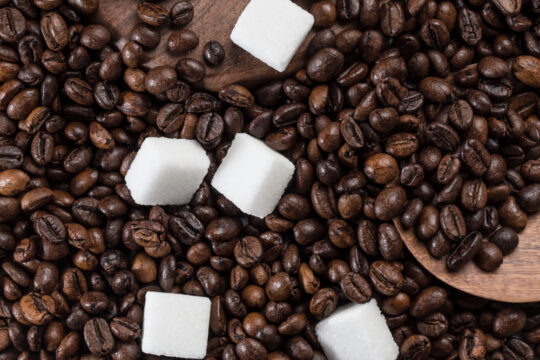 Kávészemek borítják az asztalt, rajta 5 darab kockacukor van.